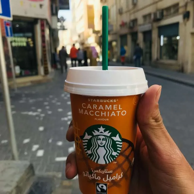 photo of a branded starbucks cup caramel machiato held up with bahrain old souq in the background
